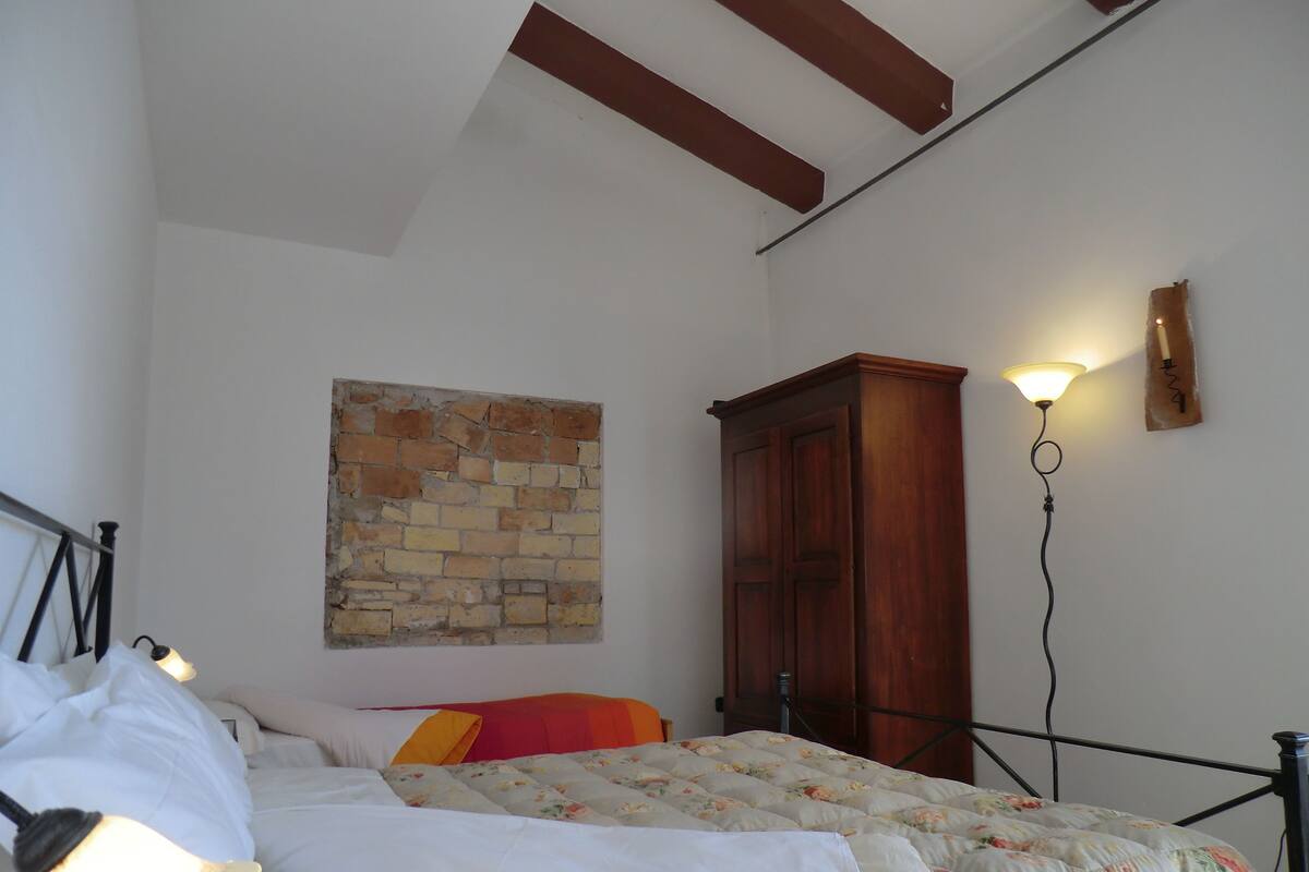 Een slaapkamer met een bed, een houten garderobe, een wandlamp en een decoratie van baksteen aan de muur.