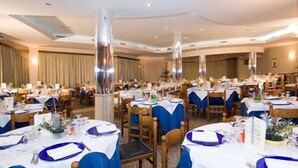 Un salón de banquetes con mesas redondas, manteles azules y sillas de madera.