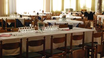 A dining area with multiple tables set for service, wooden chairs with cushioned seats, and a large window providing natural light.