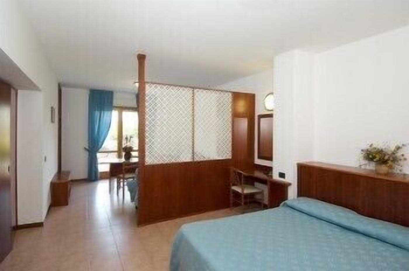 A hotel room with a bed, a desk, a chair, and a window with curtains.