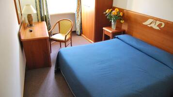 Une chambre d’hôtel avec un lit, une chaise, un bureau avec une lampe et un vase de fleurs.