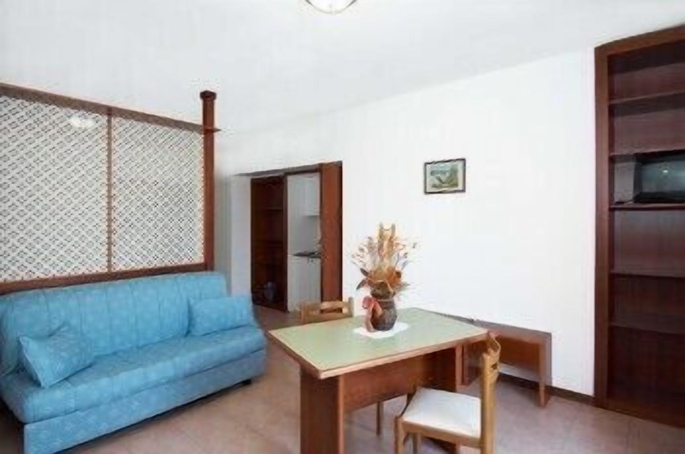 A room with a blue sofa, a wooden dining table with a chair, a small potted plant, and a wooden cabinet.