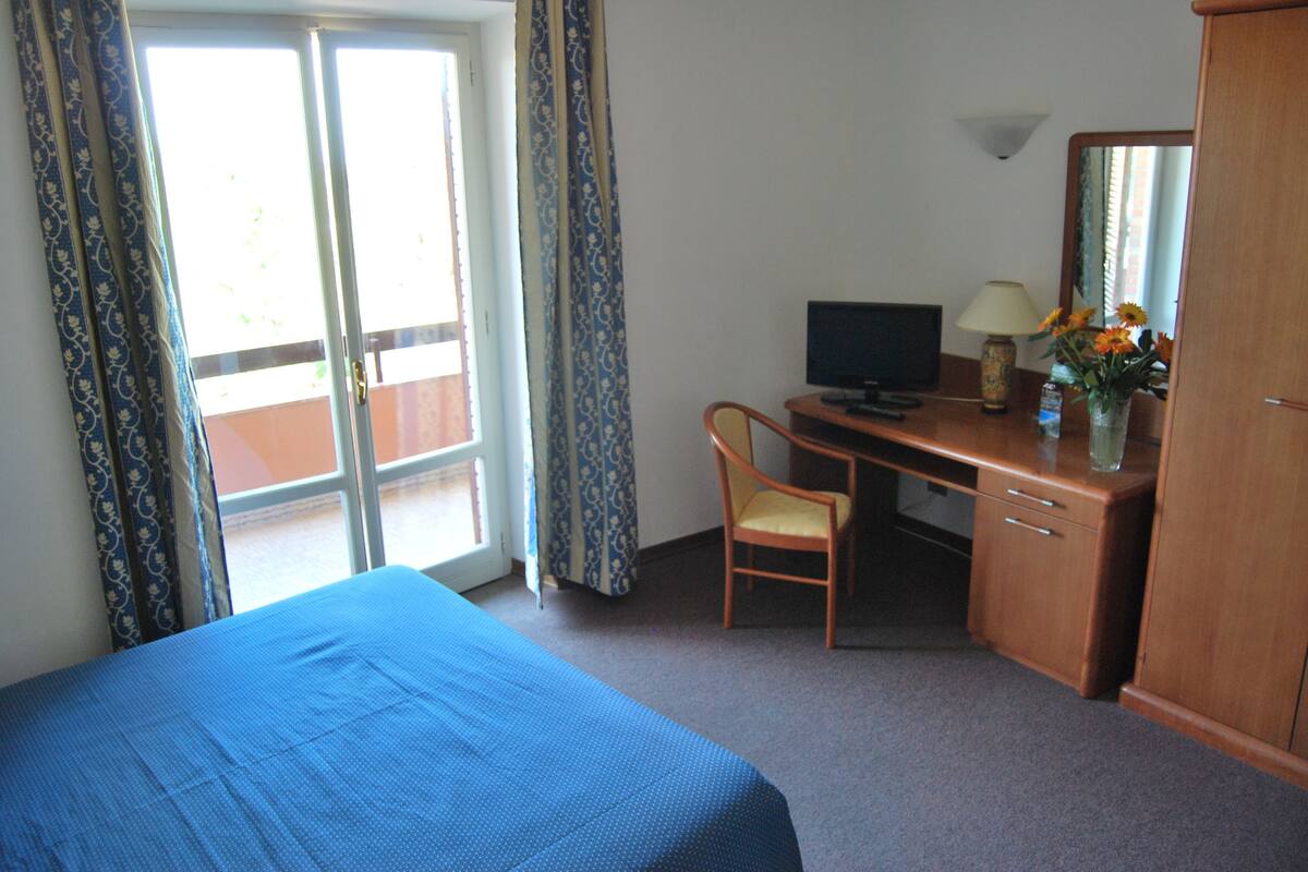 Een hotelkamer met een bed, een bureau met een computer, een stoel, een lamp en een spiegel.