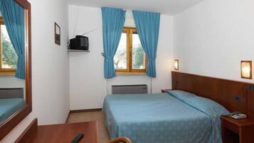 Quarto de hotel com cama, escrivaninha, cadeira, televisão e janela com cortinas.