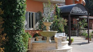 Una fuente con un cartel que indica 'Hotel Piscina' y un edificio con un letrero que dice 'Ristorante'.