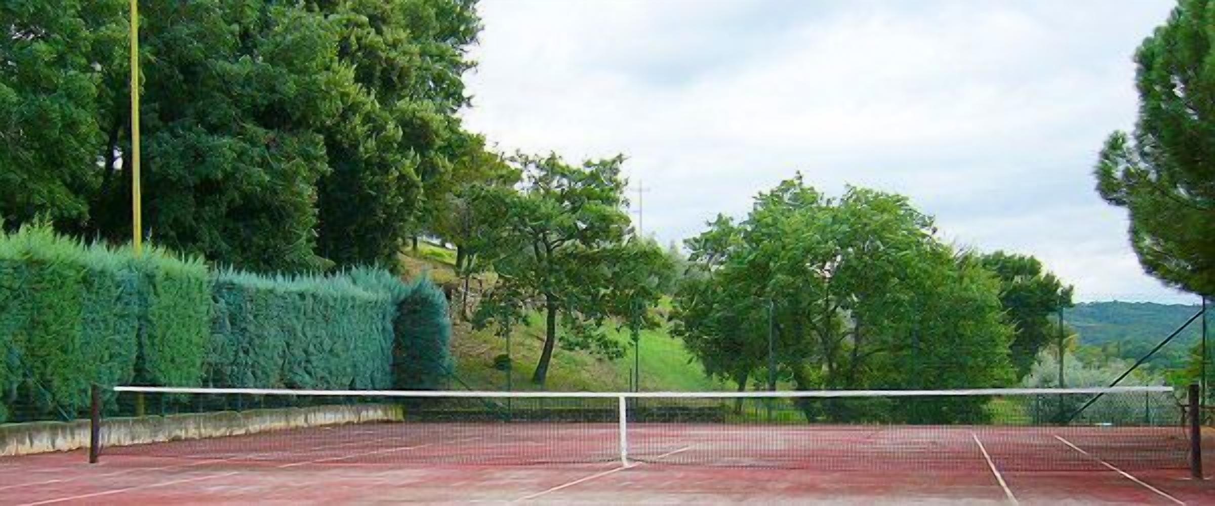 Ein Tennisplatz mit Netz, umgeben von dichten grünen Bäumen und einer Hügelkulisse im Hintergrund.