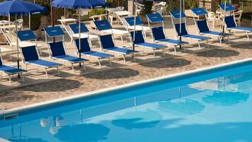 Zona junto a la piscina con sillas de descanso y sombrillas.
