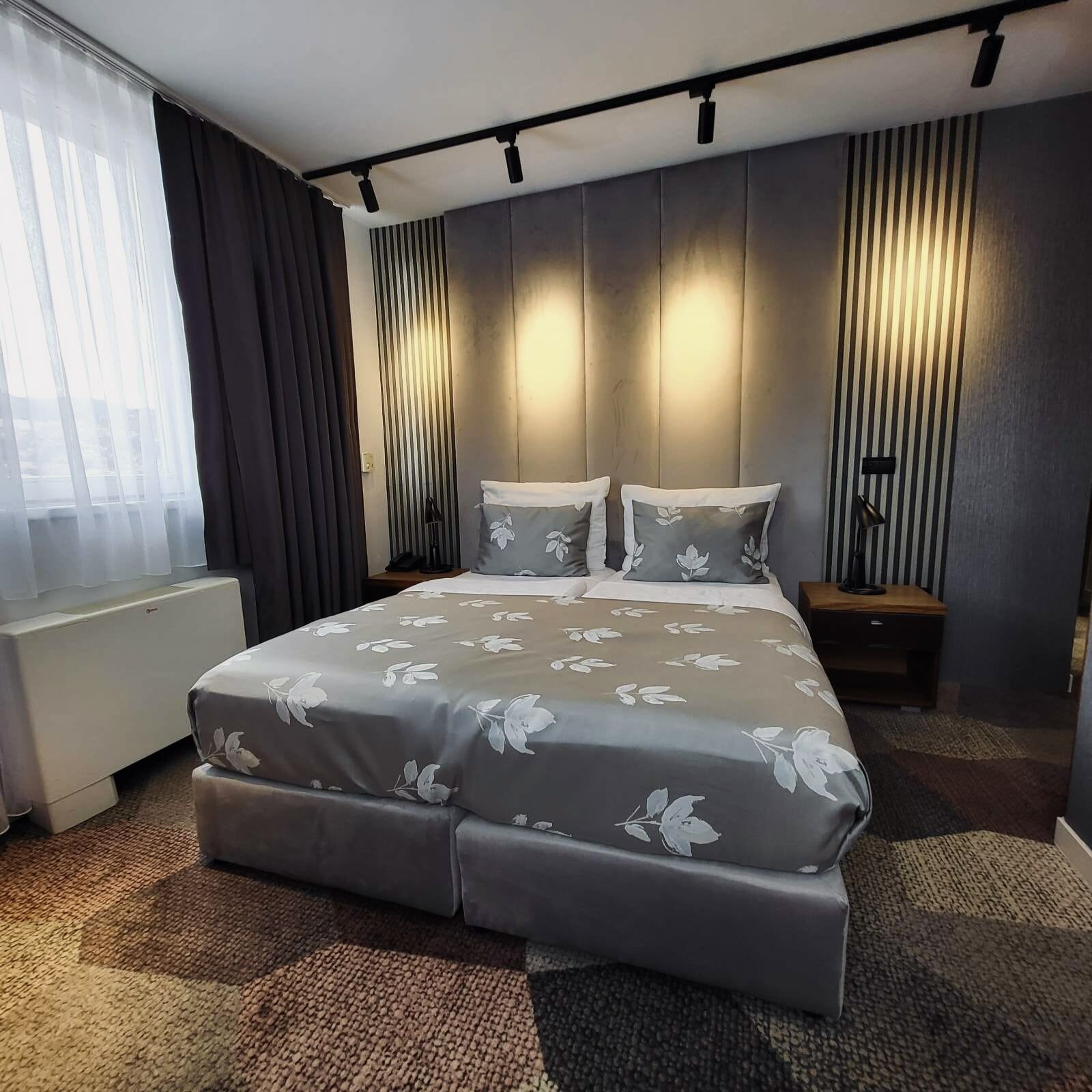 A modern hotel room with a large bed, a bedside table, a lamp, and a view of the outdoors through the window.