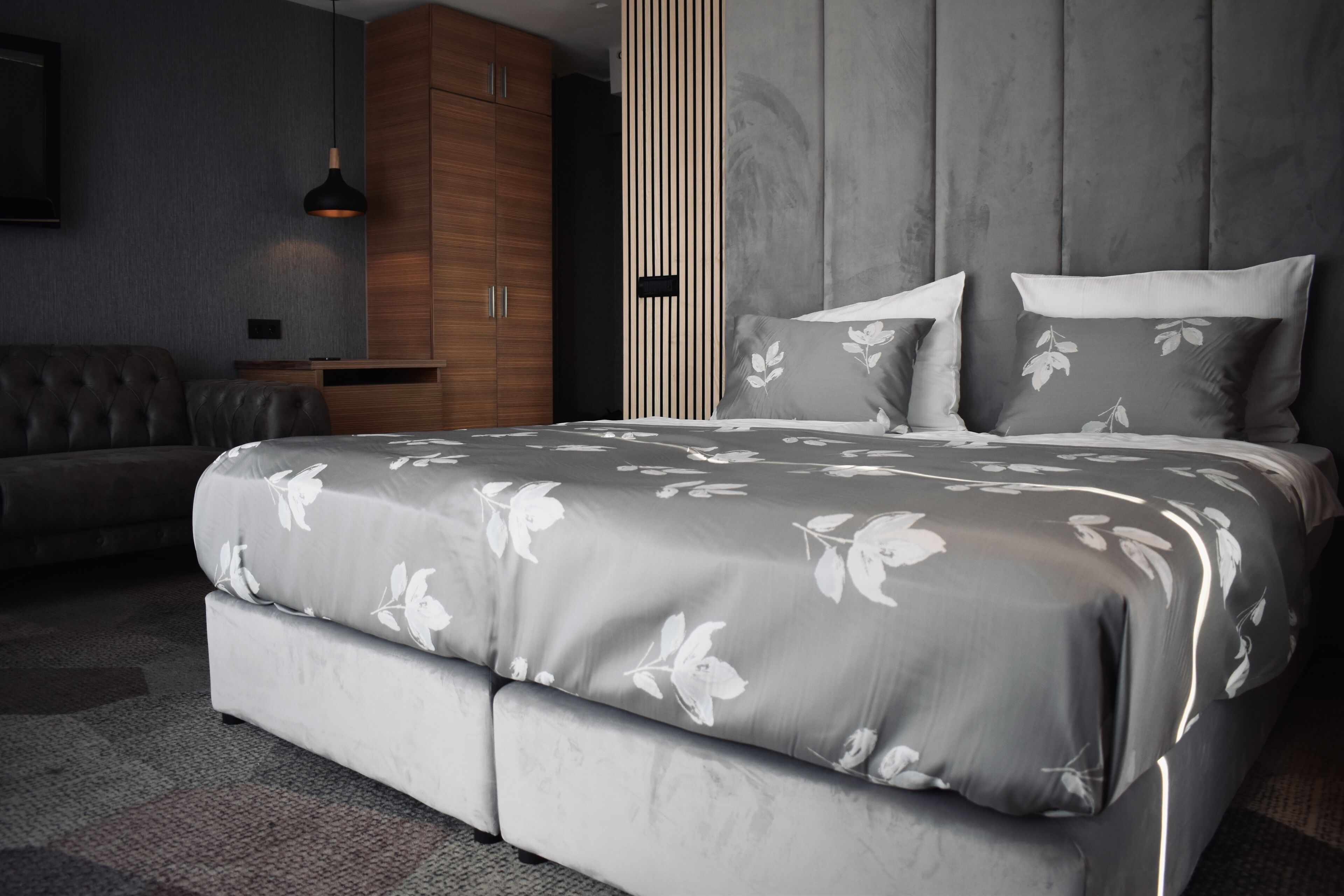 Een moderne slaapkamer met een groot bed, een houten garderobe en een grijze gestoffeerde bank.