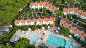 A residential complex with multiple white buildings, red-tiled roofs, and solar panels. There is a swimming pool with lounge chairs and umbrellas. - Union Lido Art & Park Hotel (Cavallino-Treporti)