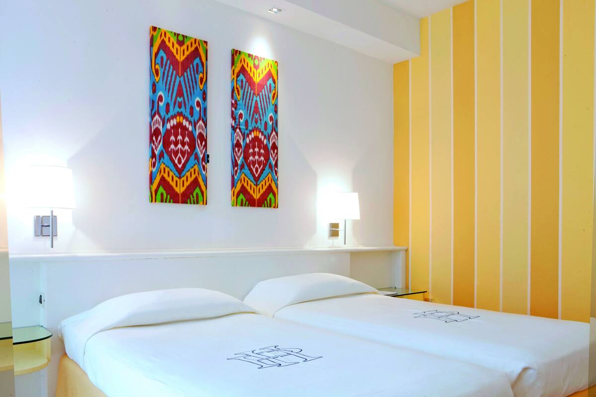 A hotel room with a bed, two wall-mounted paintings, and a yellow-striped wall.