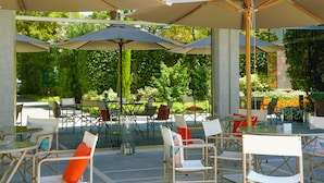 An outdoor cafe with tables and chairs, umbrellas, and greenery in the background. - Union Lido Art & Park Hotel (Cavallino-Treporti)