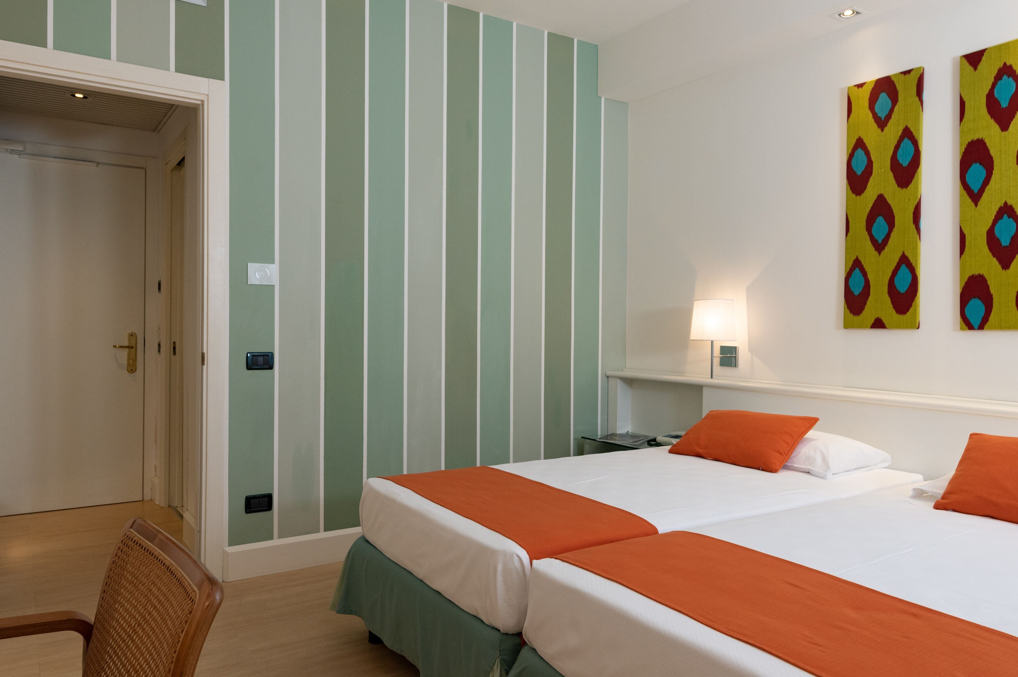 Camera d'albergo con due letti, carta da parati a righe e una piccola scrivania con una lampada.