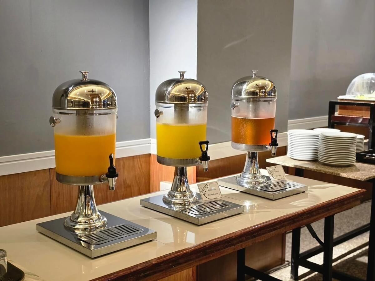 A buffet setup with three beverage dispensers on a counter, each with a different colored drink.