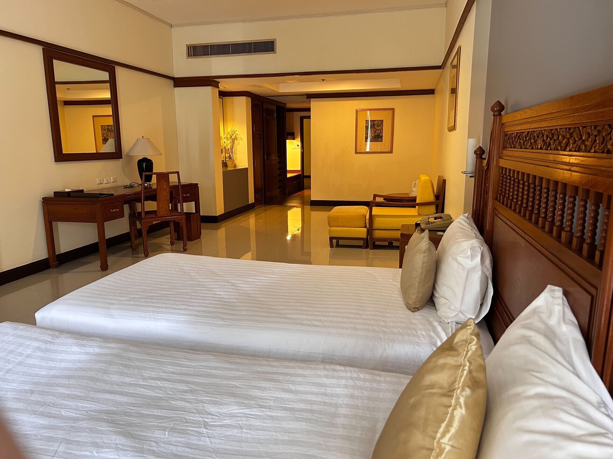 A hotel room with two beds, a desk, a chair, a mirror, and a framed picture on the wall.