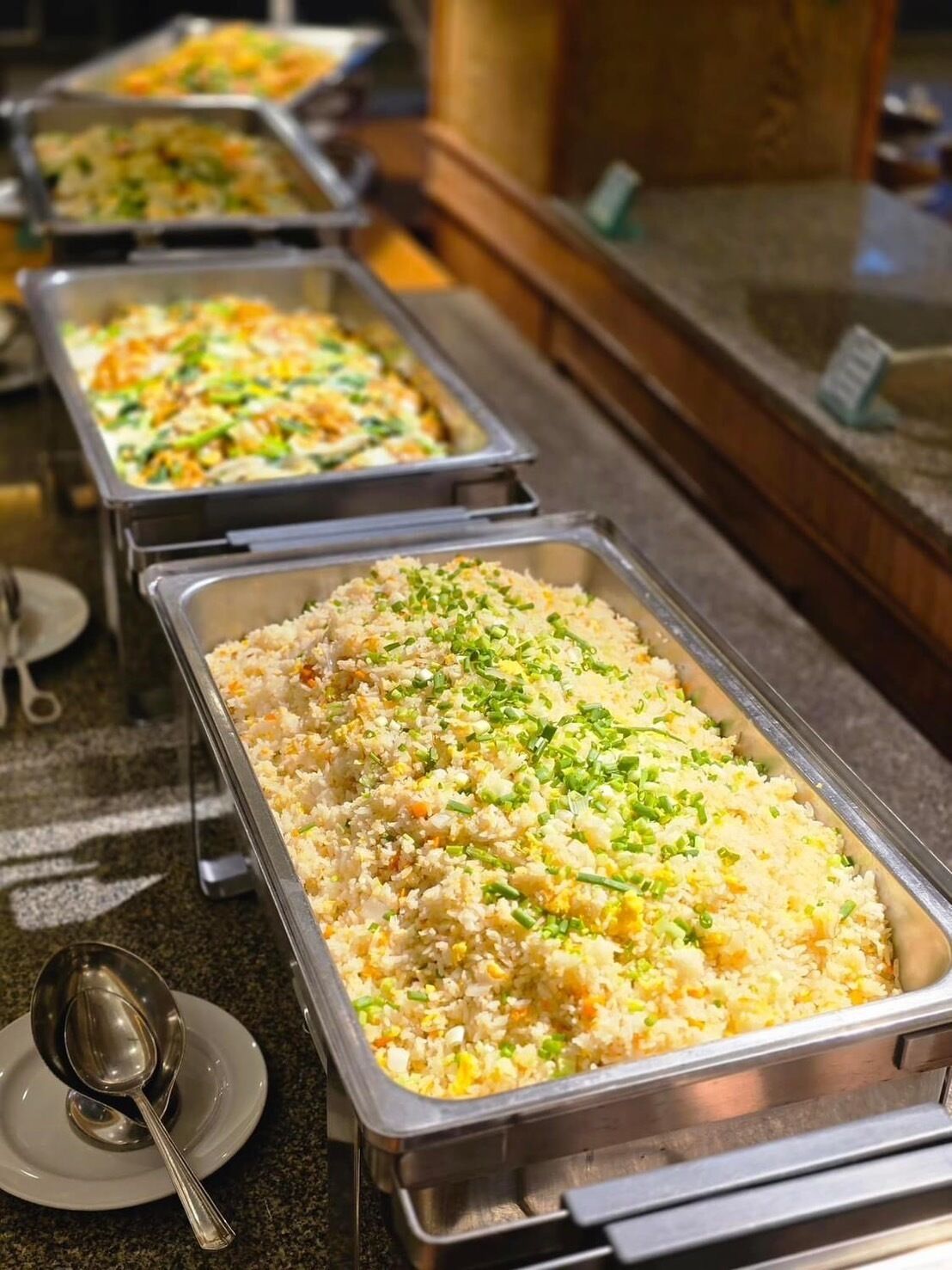 A buffet line with various dishes, including a large container of fried rice garnished with green onions.