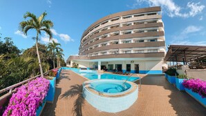 A hotel with a curved facade, outdoor swimming pool, and surrounding tropical plants.