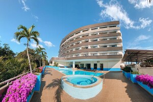 A hotel with a curved facade, outdoor swimming pool, and surrounding tropical plants.