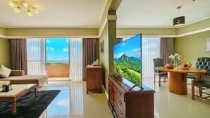 Un salón amplio con un televisor de pantalla plana grande, un sofá, una mesa de comedor con sillas y un balcón con cortinas.