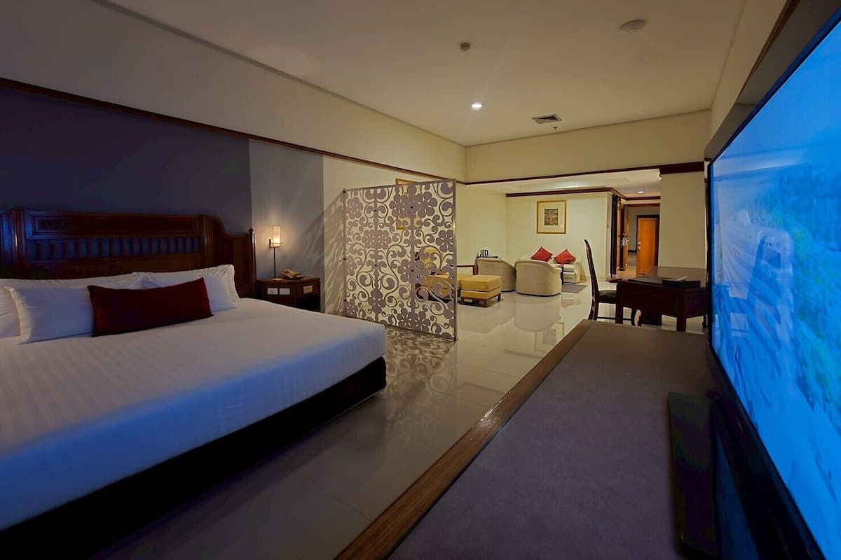 Habitación de hotel con una cama grande, televisor, zona de estar con sofás y una mesa de comedor.