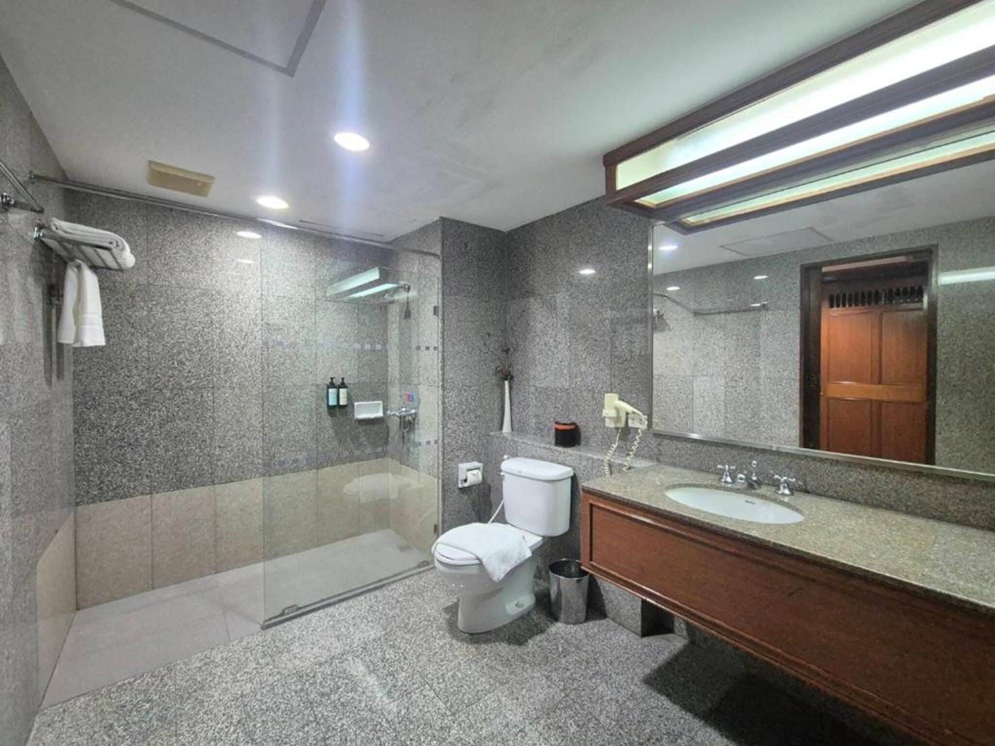 Un baño moderno con ducha envuelta en vidrio, inodoro blanco y tocador de madera con lavamanos.