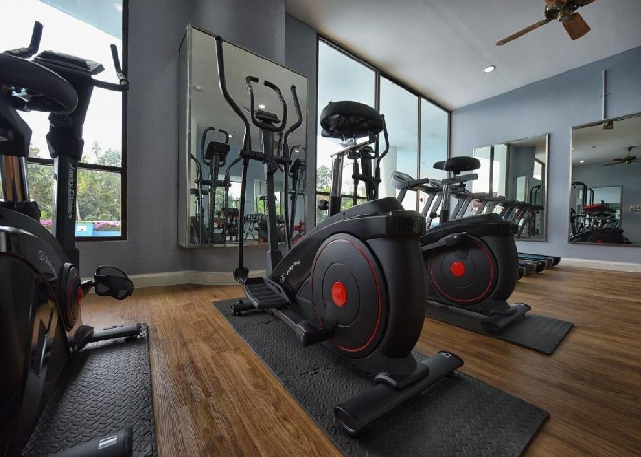 Een fitnessruimte met cardioapparatuur, spiegels en grote ramen.