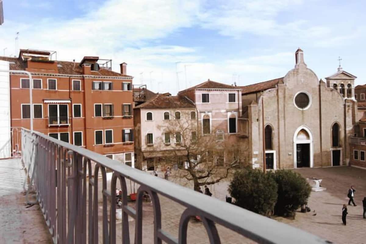 Un patio con edificios históricos, una iglesia y un balcón con baranda de metal.