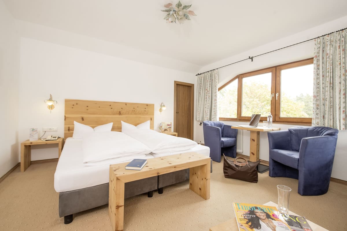 A hotel room with a wooden bed, a desk with a laptop, a chair, and a bench.