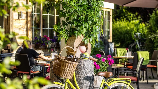 A yellow bicycle parked next to a tree with a wicker basket attached to it. - Hotel Maximilian (Ehenbichl)