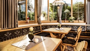A cozy restaurant with wooden furniture, large windows, and a view of greenery. - Hotel Maximilian (Ehenbichl)