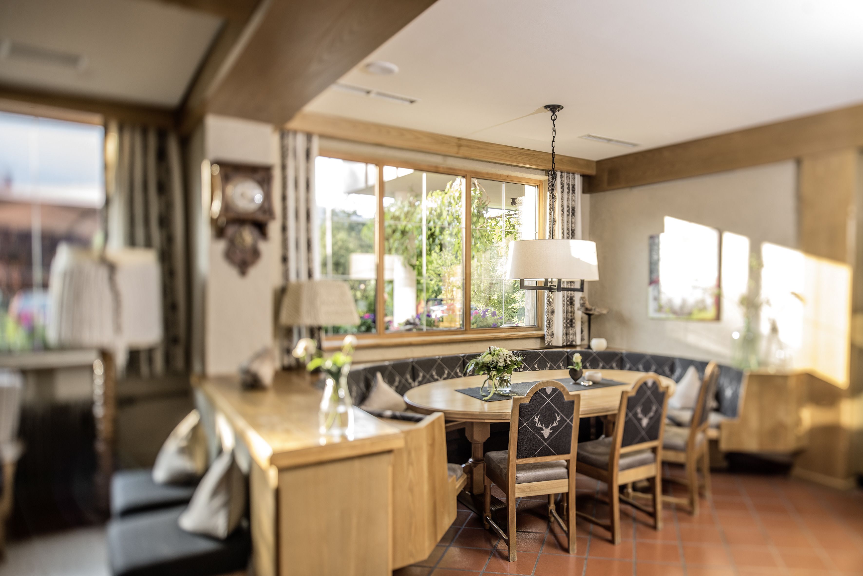 A dining area with a wooden table, chairs, and a bench. There is a window with a view of greenery outside.