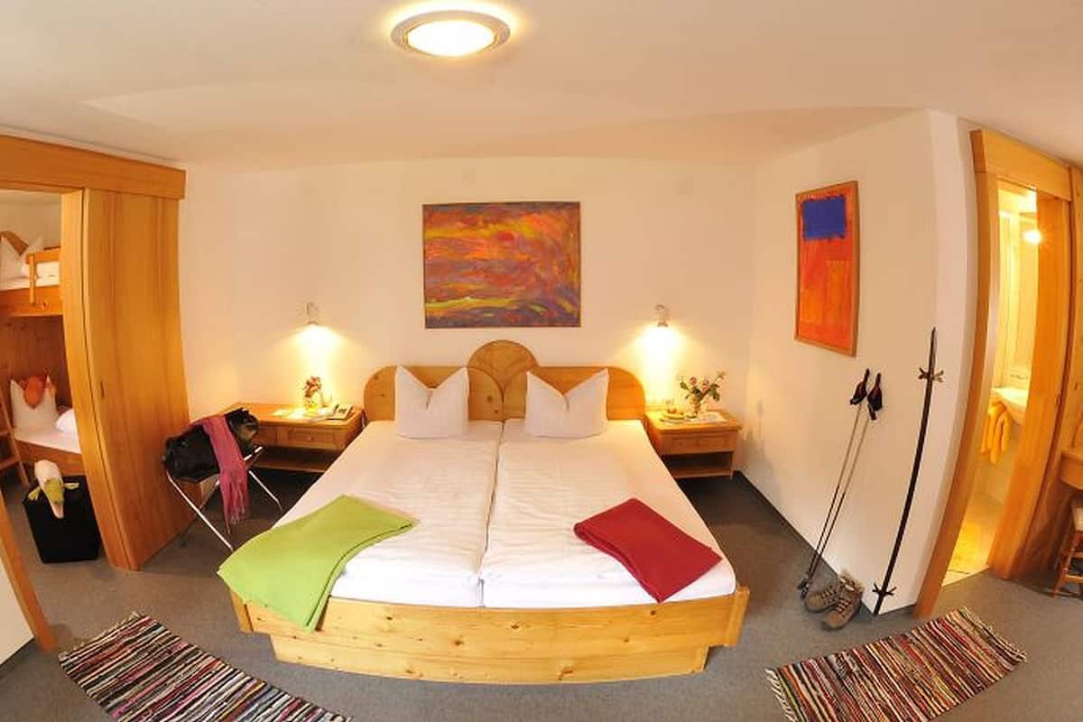 A cozy bedroom with a wooden bed, two bedside tables with lamps, a colorful painting on the wall, and a wooden wardrobe.