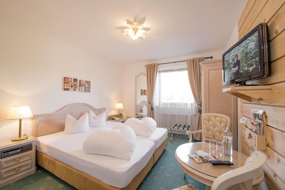 A hotel room with a bed, bedside tables, a desk, a chair, a television, and a mirror.