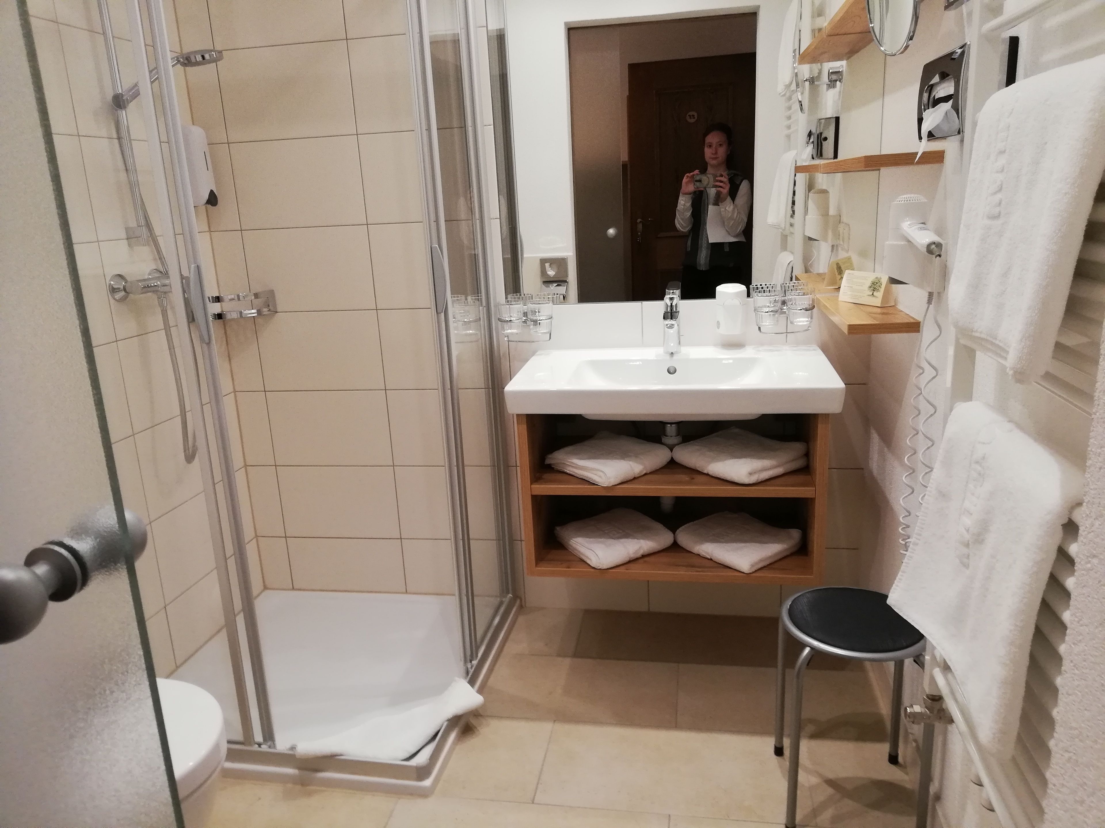 A modern bathroom with a glass shower enclosure, a sink with a mirror, and a shelf with folded towels.