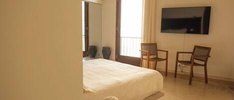 A bedroom with a bed, two chairs, a TV on the wall, and a large window.