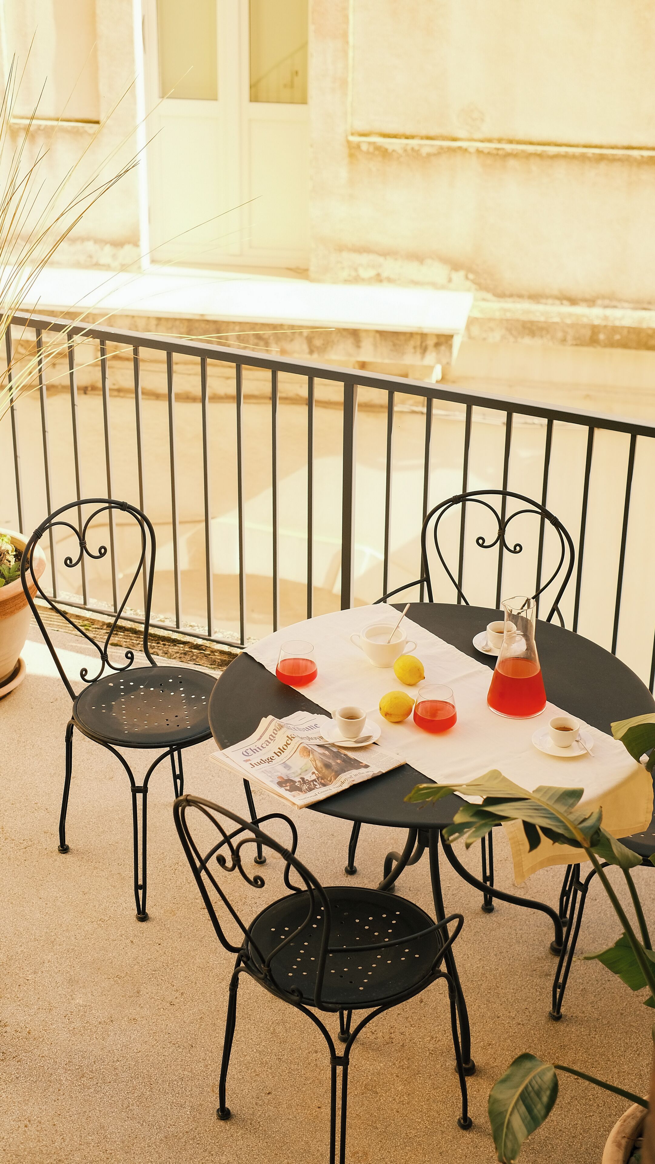 A balcony with a round table, two chairs, a potted plant, and a newspaper.