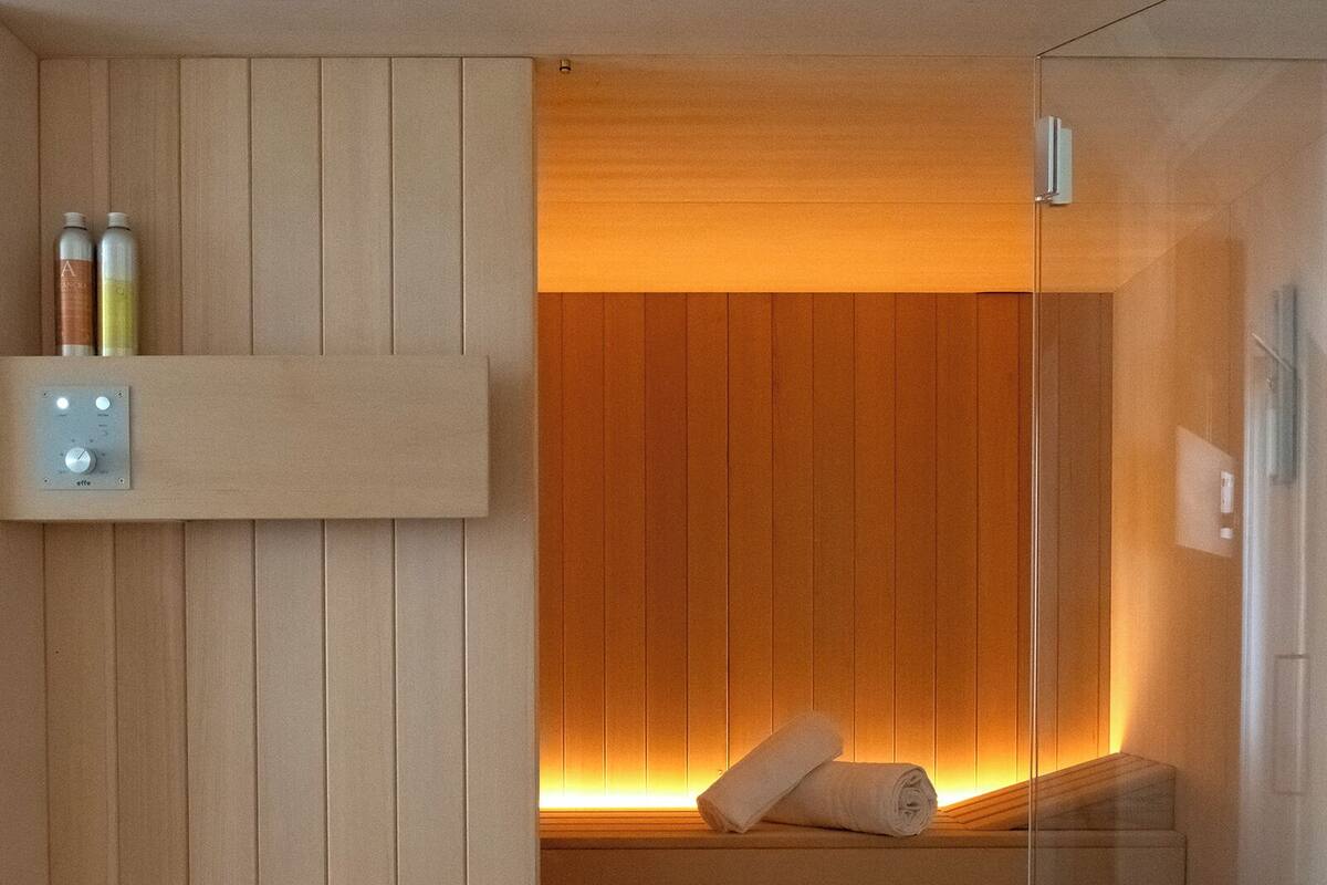 A modern spa room with a wooden bench, a glass partition, and a wall-mounted shelf with bottles.