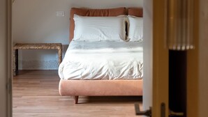 Un dormitorio con techo de madera, cama con ropa de cama blanca y marrón, y un pequeño banco.