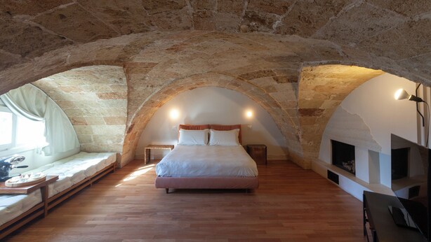 Un dormitorio con techo abovedado de piedra, una cama, una mesita con una lámpara y una chimenea.