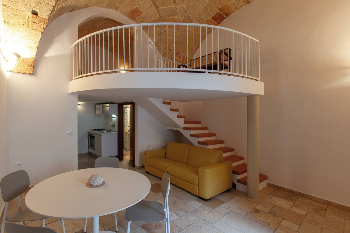 A modern interior with a white dining table, a yellow sofa, and a staircase leading to an upper level.