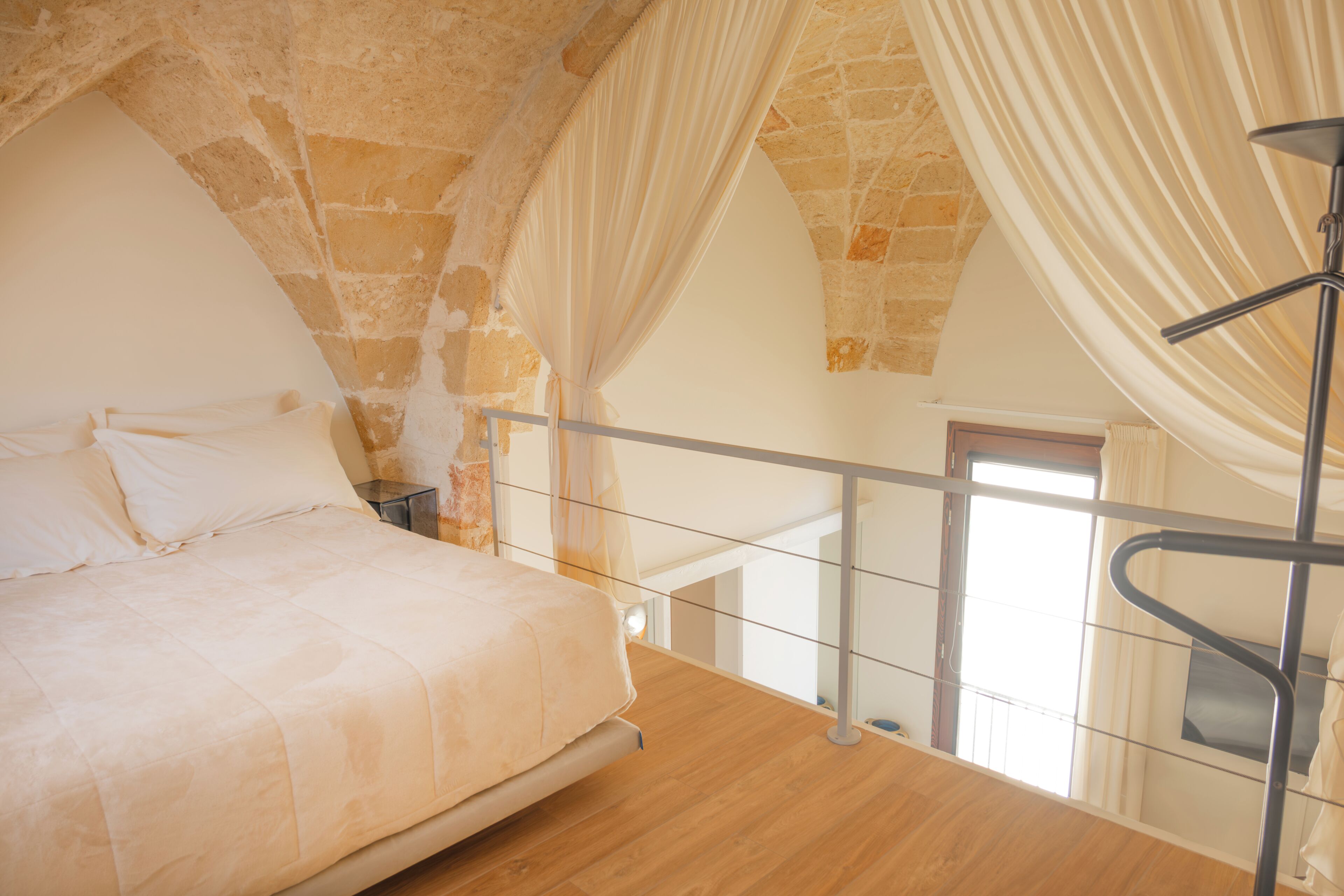 A bedroom with a bed, a nightstand, a window, and a staircase.