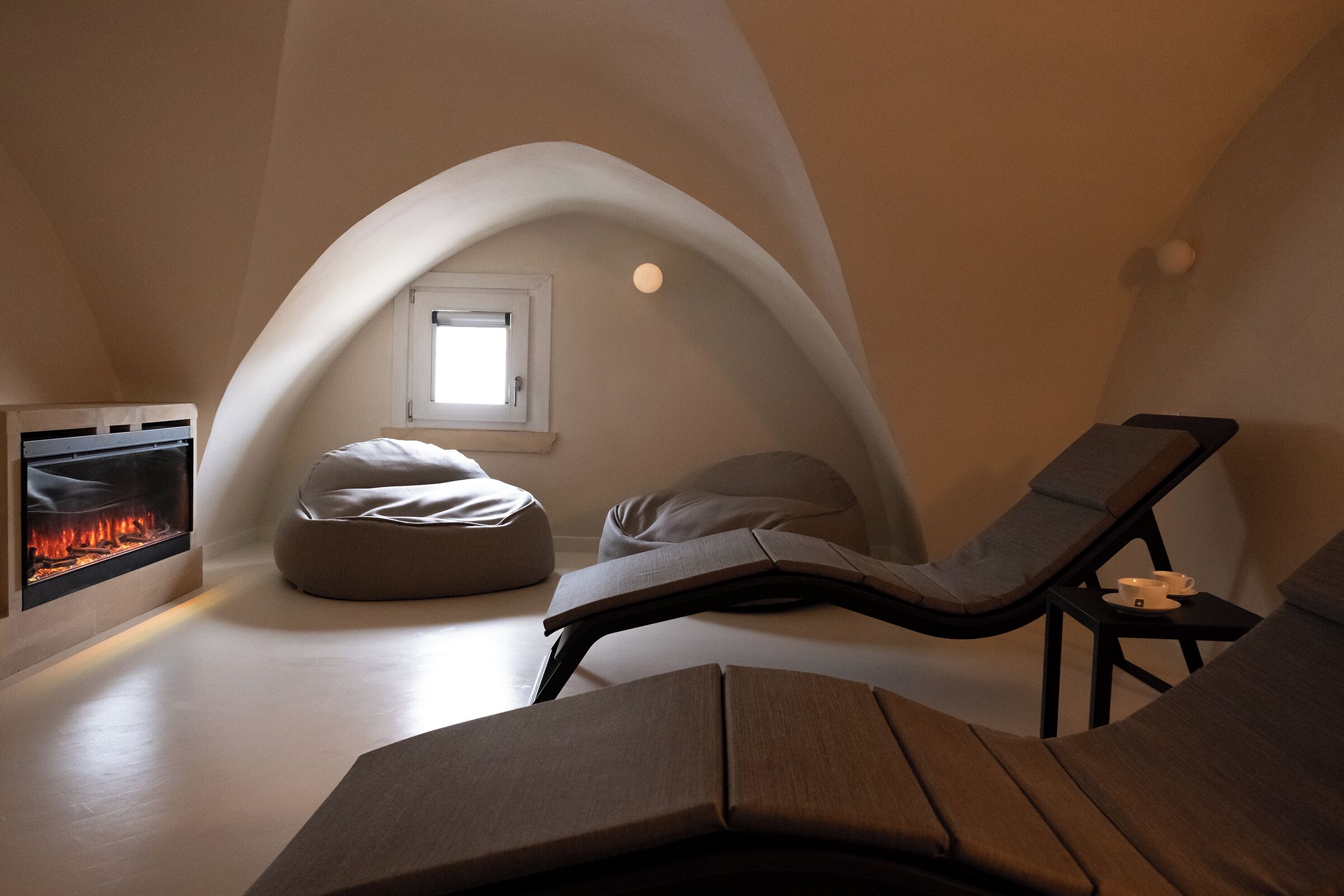 A cozy, modern room with a fireplace, a comfortable lounge chair, and a small window.