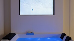 Habitación con un amplio ventanal que muestra un paisaje nevado, una bañera con iluminación azul y dos altavoces a cada lado.
