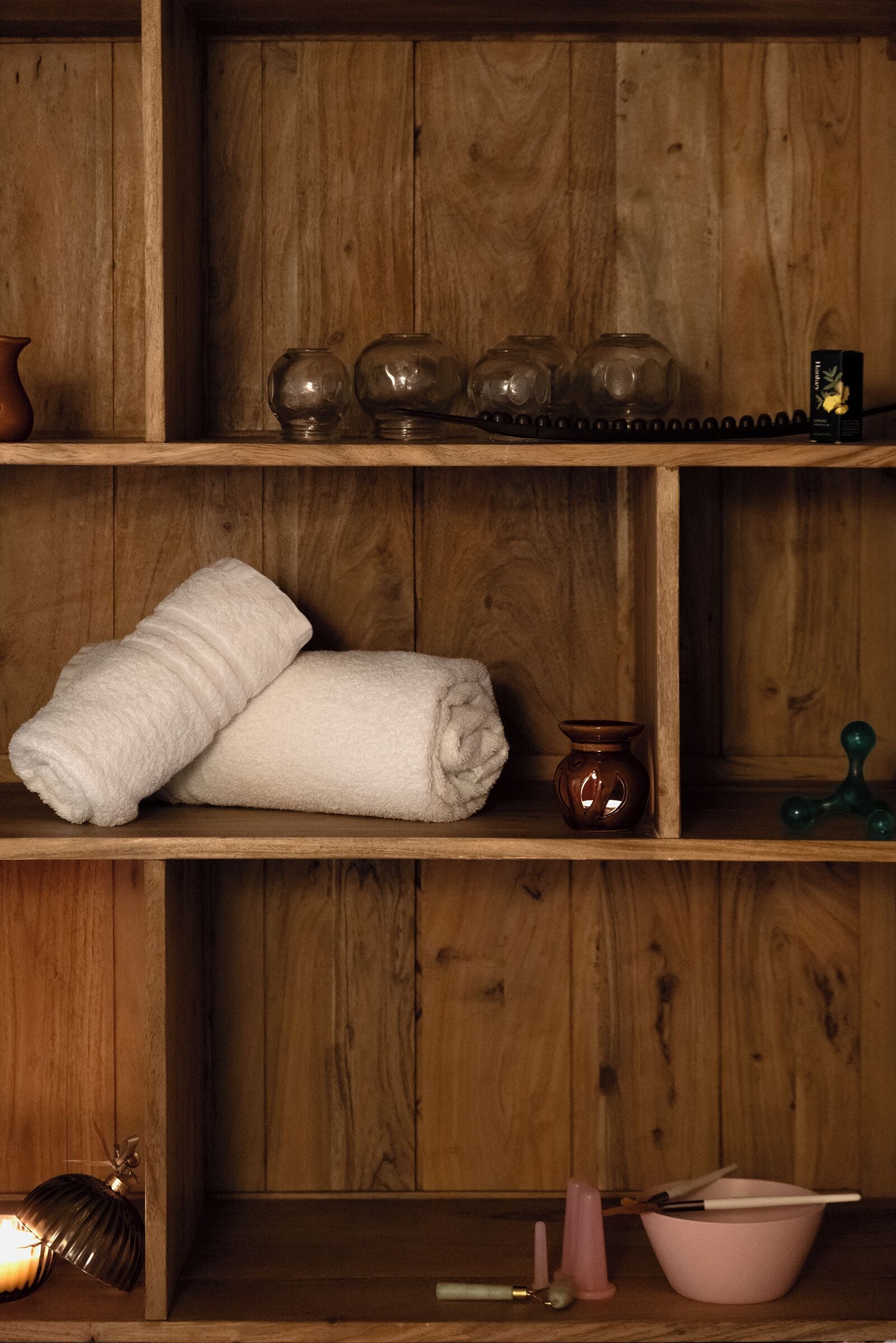 Une étagère en bois avec des serviettes, des bocaux en verre et des ustensiles de cuisine.