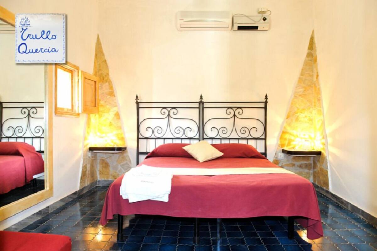 A hotel room with a bed, a mirror, and a sign that reads "Trullo Quercia".
