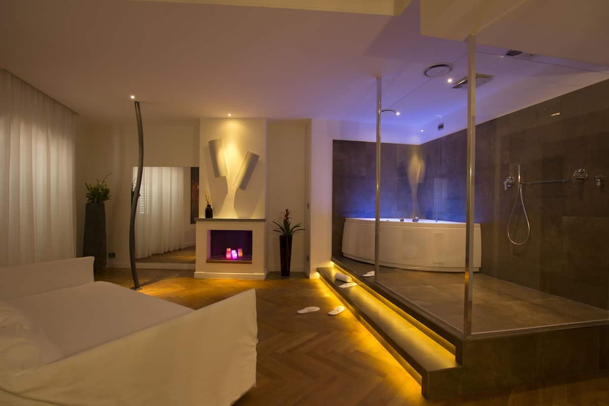A modern bathroom with a glass-enclosed shower, a bathtub, and a seating area with a fireplace.