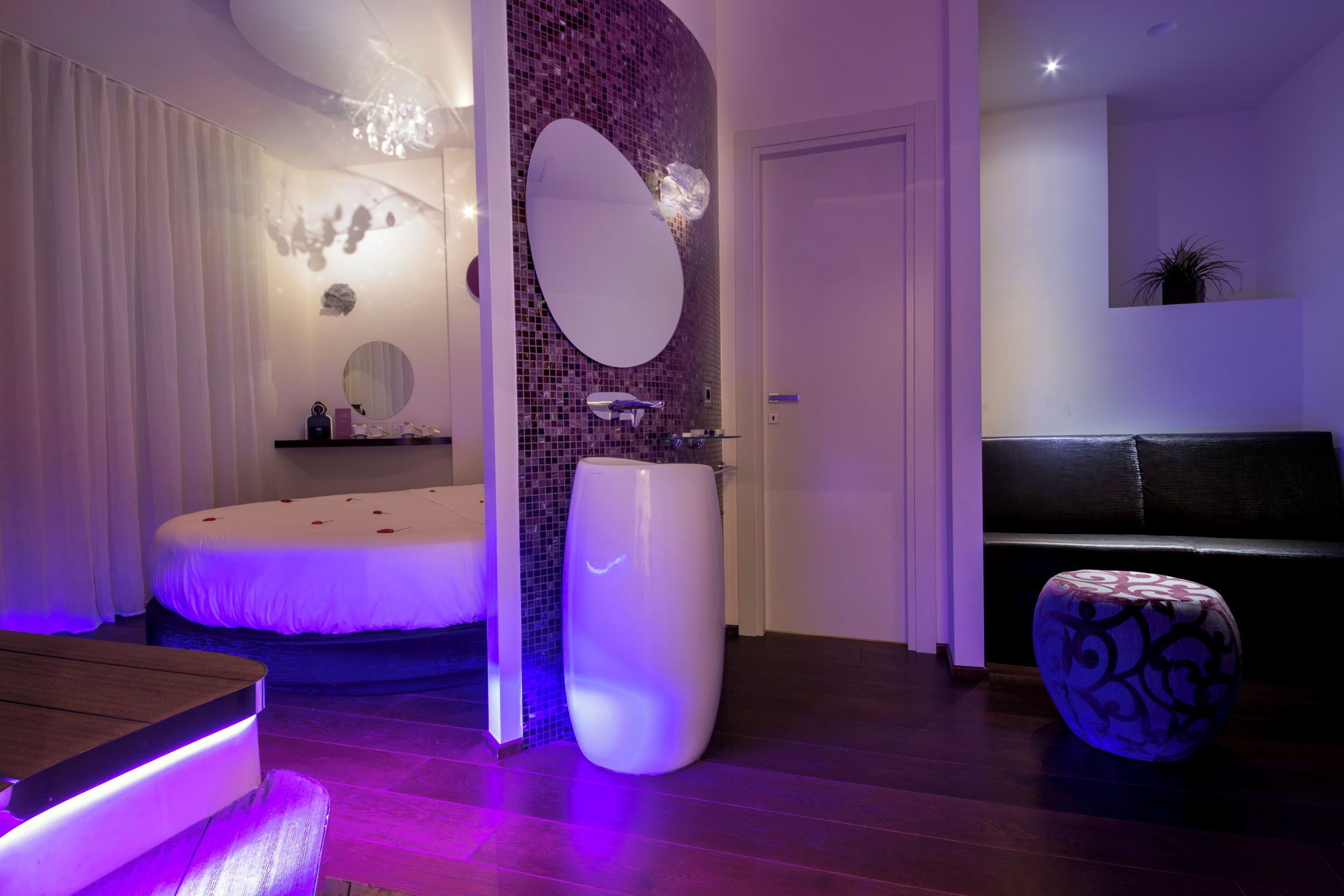 A modern bathroom with a large mirror, a round bathtub, and a white pedestal sink.