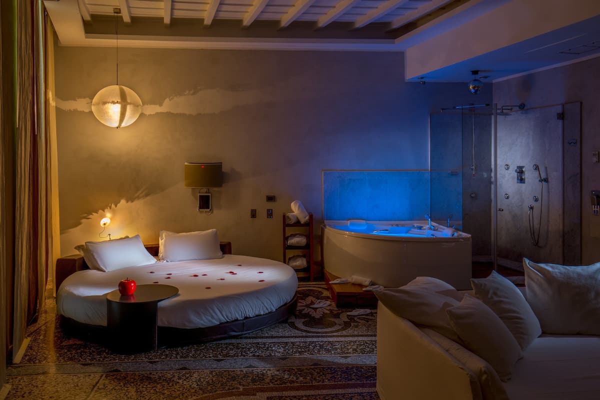 A bedroom with a bed, a sitting area, a bathtub, and a wardrobe.
