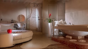 A modern bathroom with a large bathtub, a shower, and a toilet. There is a round mirror above the sink, and a potted plant on the counter.