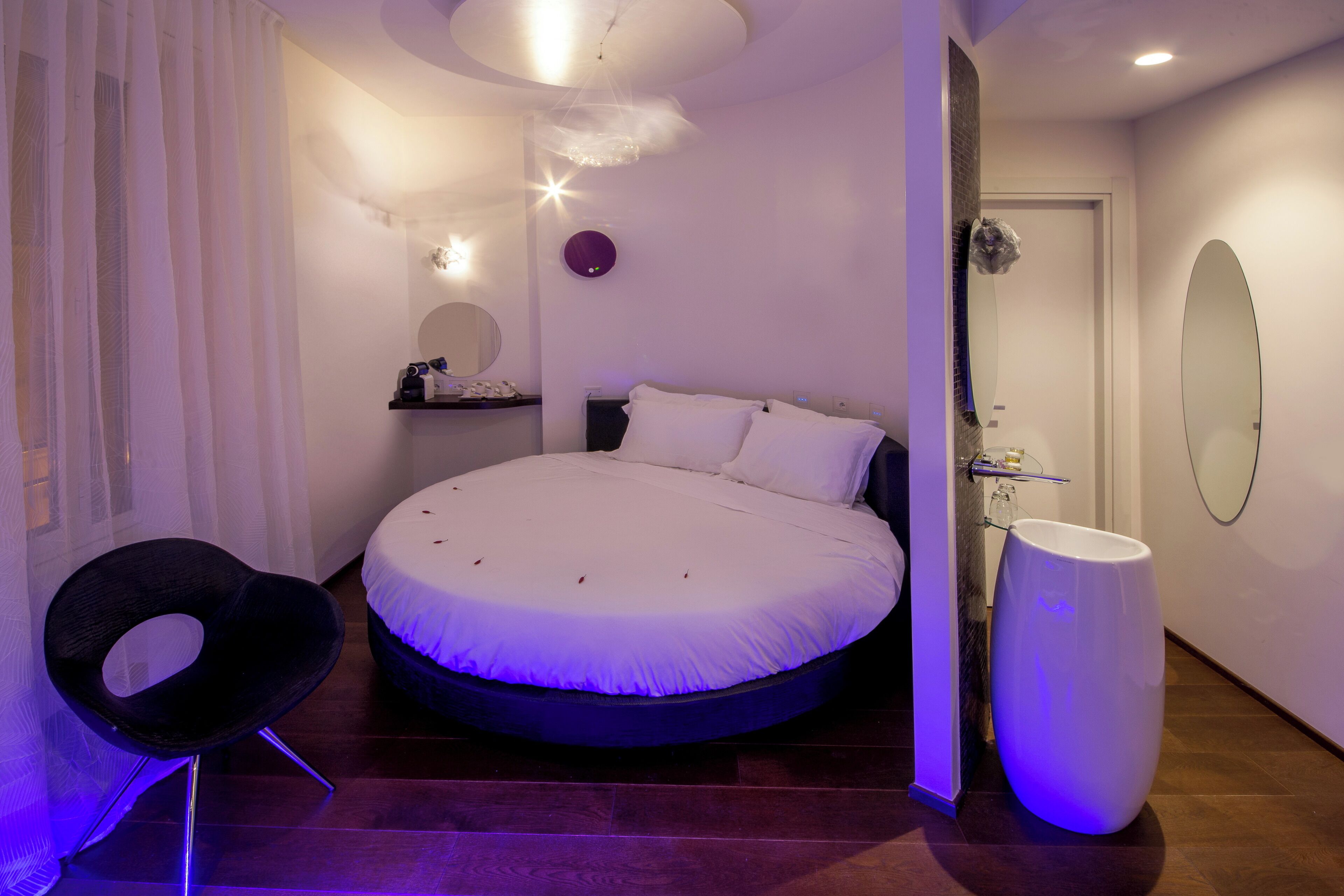 A modern bedroom with a circular bed, a round chair, a large mirror, and a unique white toilet.